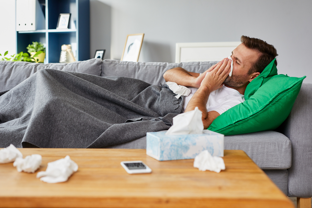 An image of a man laying on the couch and blowing his nose, clearly under the weather. Believe it or not, this is something that your local Ann Arbor chiropractor can help with.
